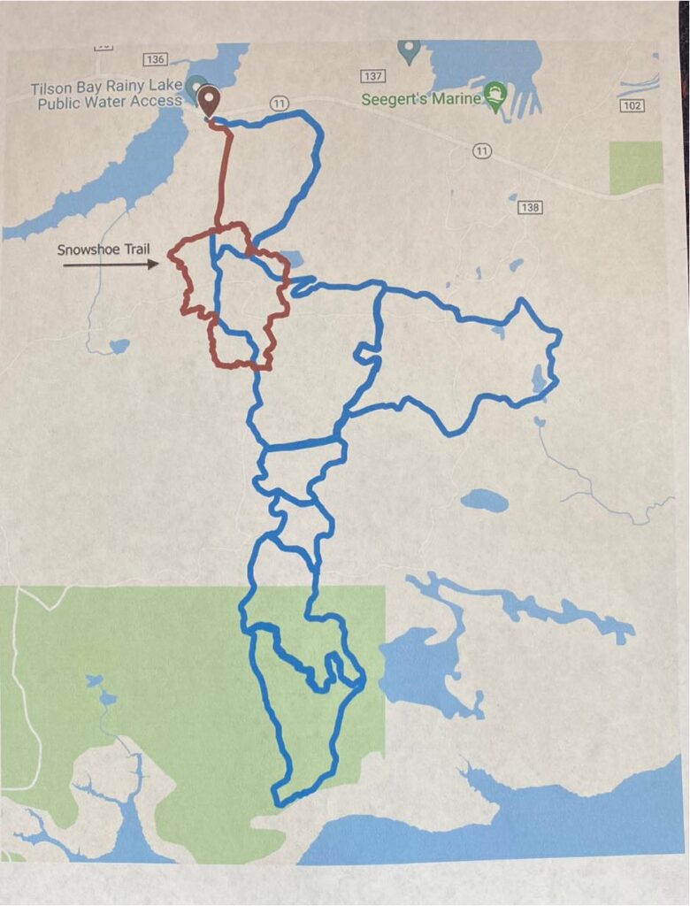 A trail map showing the Snowshoe Trail with red and blue routes near Tilson Bay, Rainy Lake, and Seegert’s Marine in Minnesota, displayed over a light background with water and forest areas. | Rainy Lake, MN