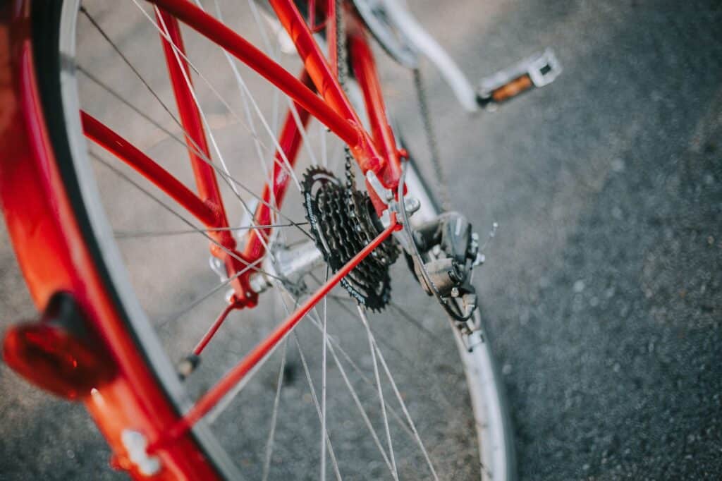 Close-up view of the rear wheel and gears of a red bicycle, with focus on the chain, derailleur, and spokes, set against a paved surface in Minnesota near Rainy Lake. | Rainy Lake, MN