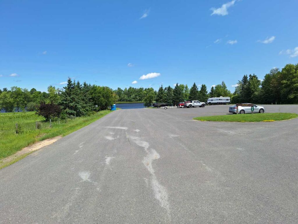 Large, mostly empty parking lot with a few cars parked near the back, surrounded by green trees under a clear blue sky with some clouds—offering easy Vidas Access for all visitors. | Rainy Lake, MN